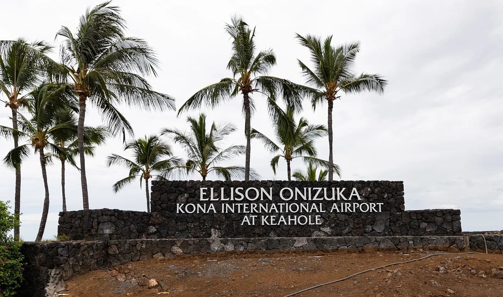 Lava-rock entrance sign for Ellison Onizuka Kona International Airport at Keahole, with coconut palms
