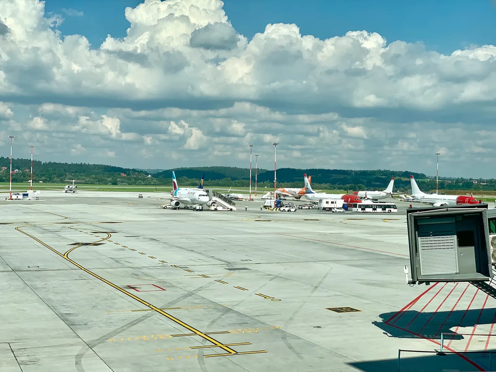 Airport apron, jet bridges, and parked aircraft seen through large windows from inside the Kraków-Balice passenger terminal.