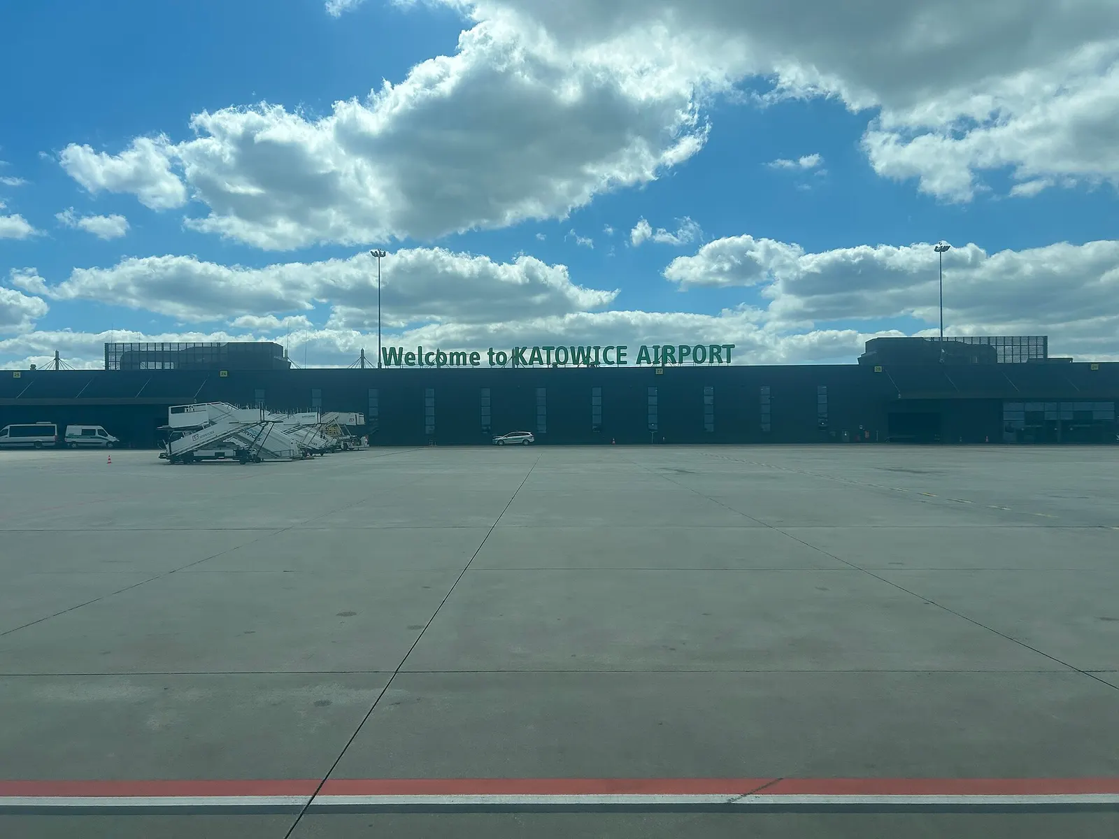 A view from a passenger airport bus after landing, showing the terminal, ramp equipment, and service vehicles on the apron.