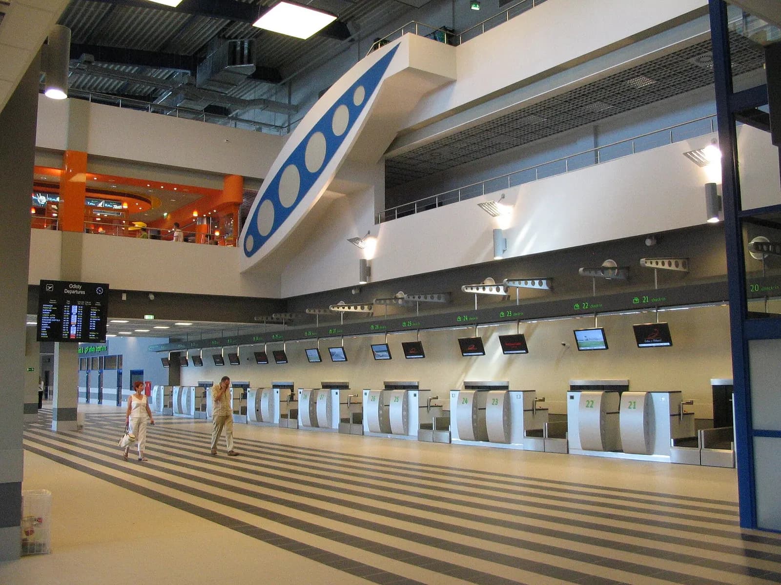 A row of check-in counters in Terminal B at Katowice Airport with airline desks and the departures hall stretching behind them.