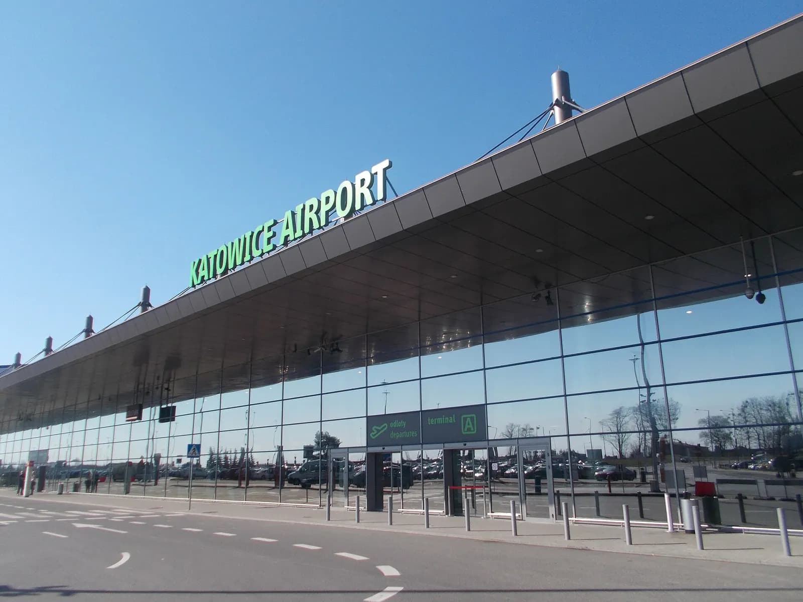 The exterior facade of Terminal A at Katowice Airport seen from the forecourt, with entrance doors and drop-off area in front.