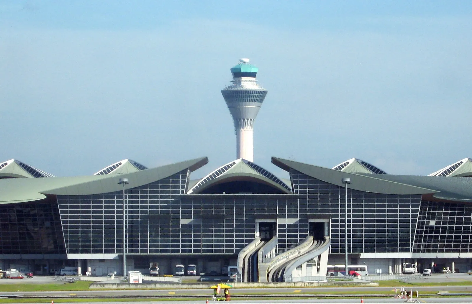 The curved white roof and tall control tower of KLIA's Main Terminal Building stand against open sky and landscaping.