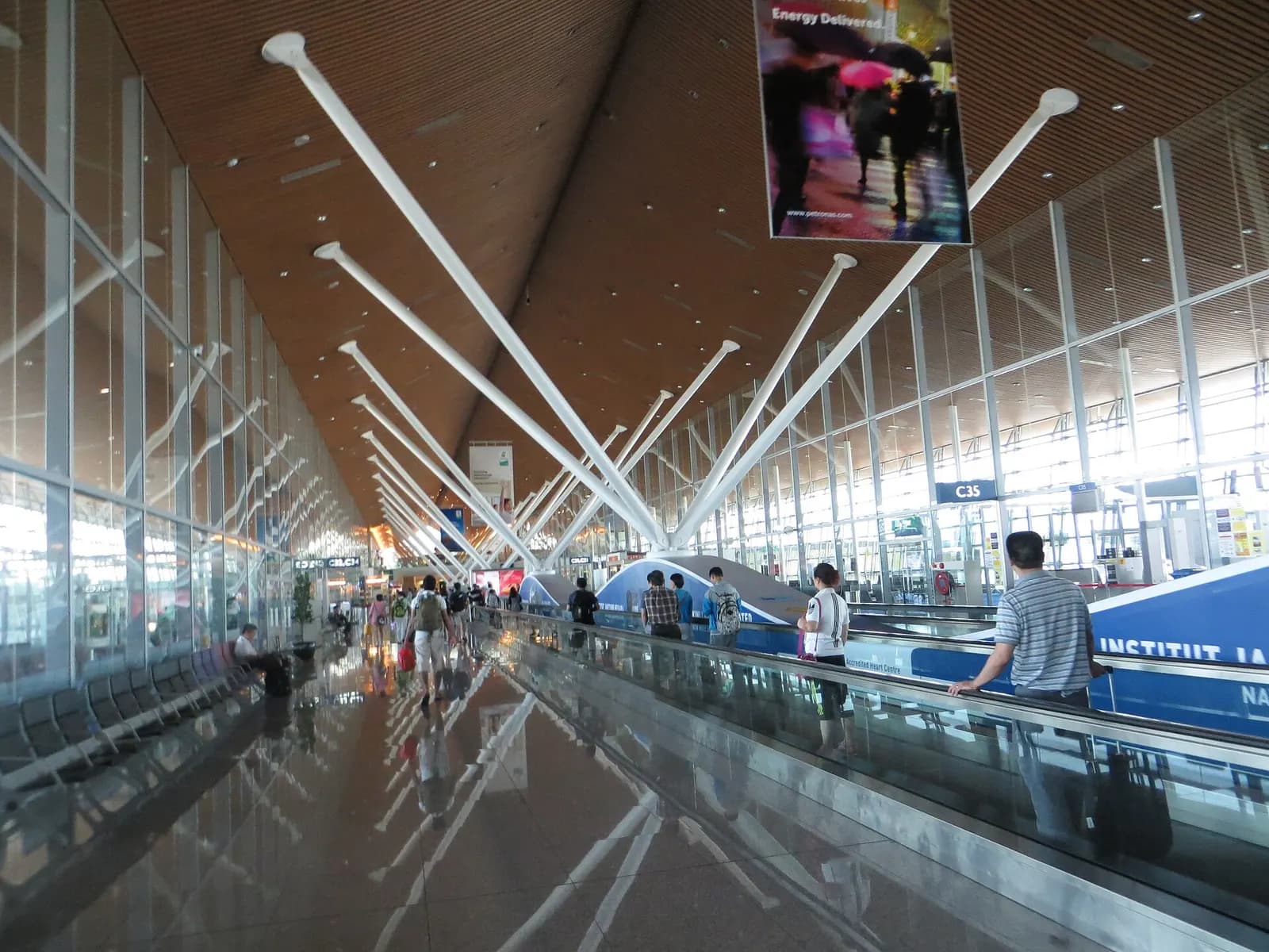 A long, bright concourse in the Satellite Terminal with high ceilings, shops, and gate areas stretching down both sides.