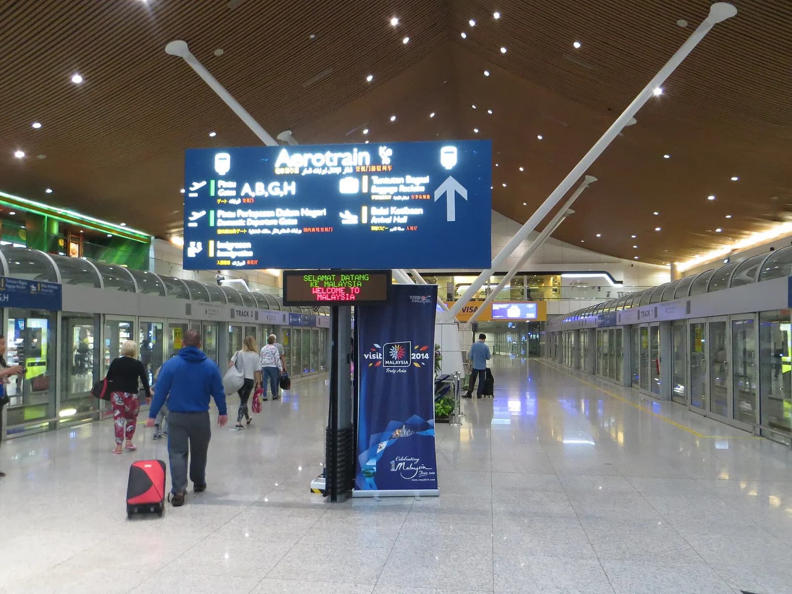 Passengers wait on the platform of the Satellite Terminal Aerotrain station behind glass walls and railings.