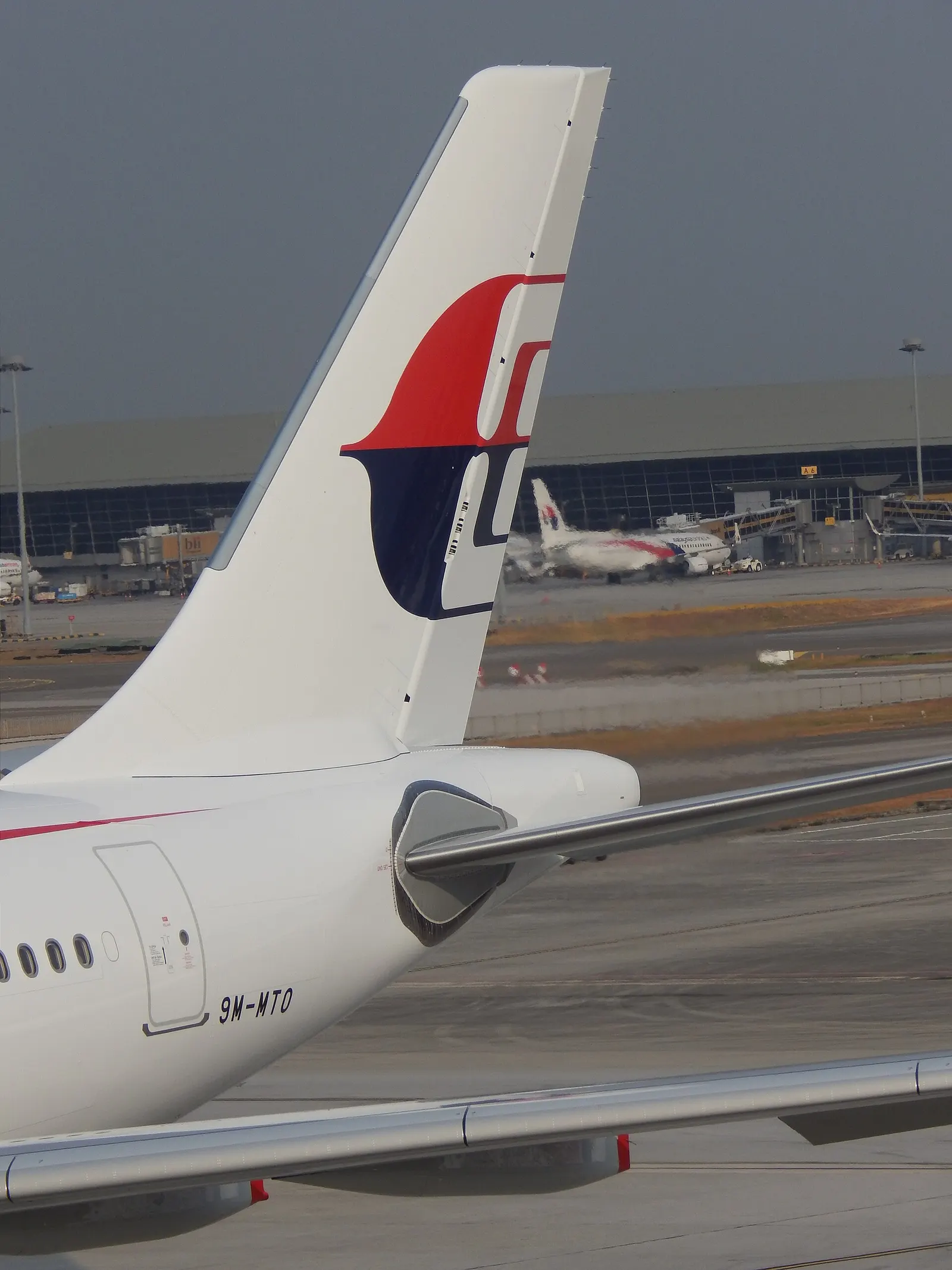 A Malaysia Airlines Airbus A330 sits on the international remote apron with terminal buildings visible across the airfield.