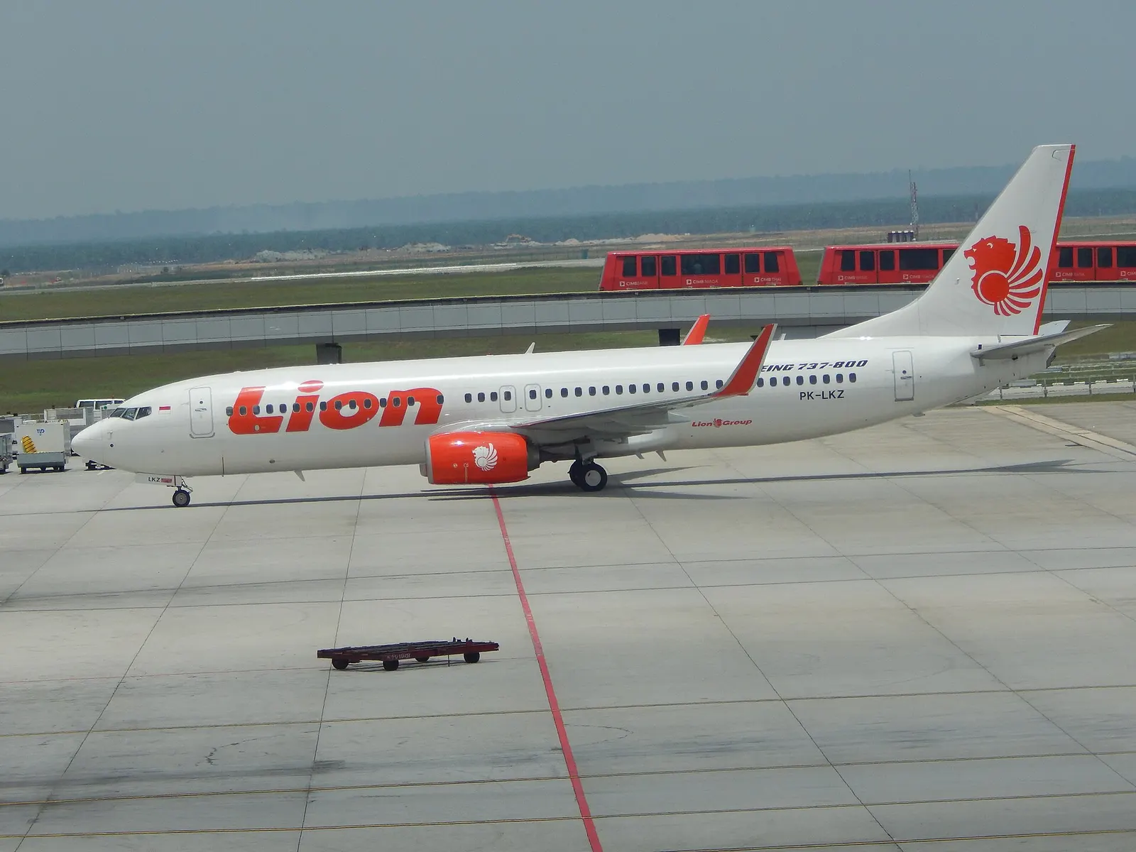 A Boeing 737 taxis to a remote stand while the elevated Aerotrain passes on its track in the background.