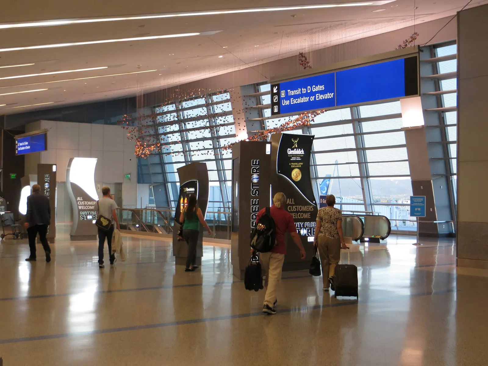 Bright Terminal 3 concourse with escalators leading down toward the tram connection to D Gates.