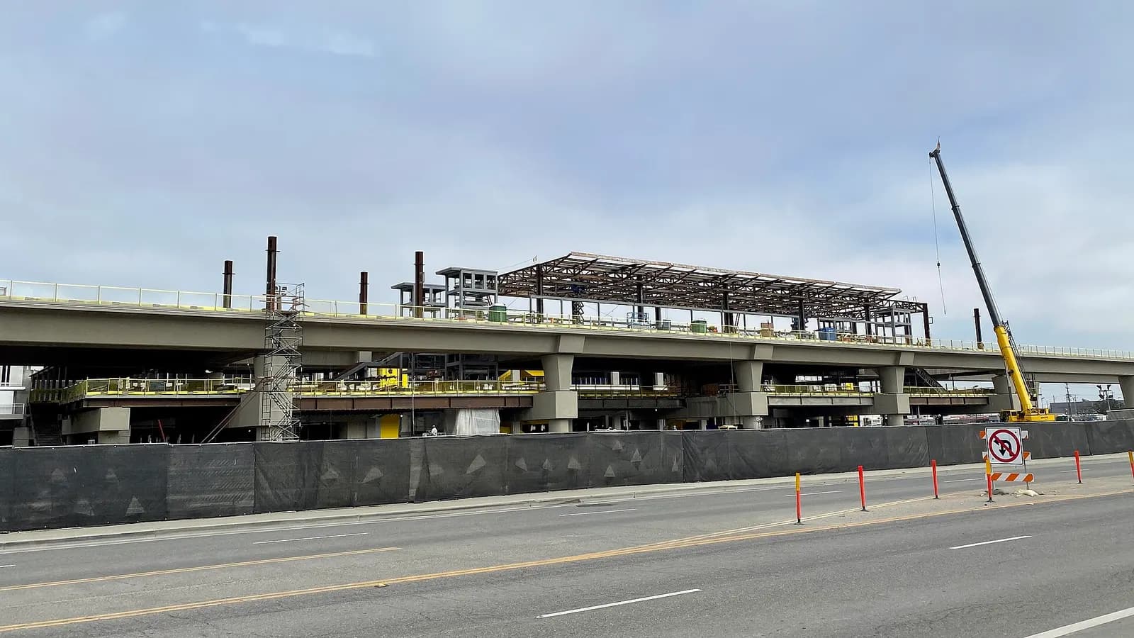 The elevated guideway and station structure of the LAX Automated People Mover under construction, with cranes and the terminal area visible beyond.