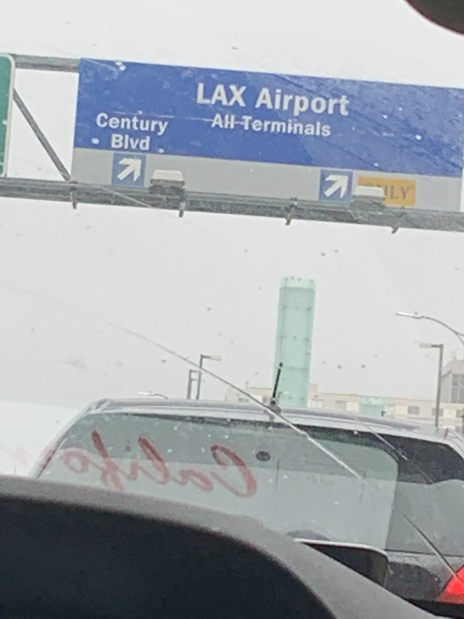 A wide view of LAX's horseshoe-shaped terminal complex and the Century Boulevard exit road, with multiple terminals visible from an elevated vantage point.