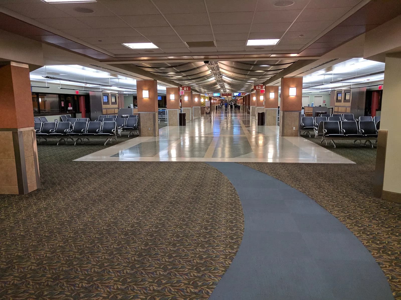Empty Blue Grass Airport holdroom with a curved blue walkway and rows of black seats, photographed in September 2017.