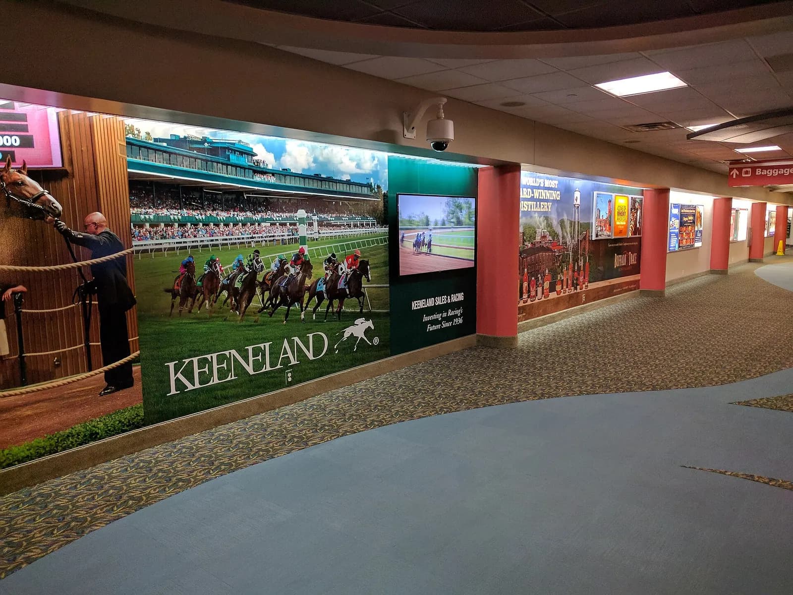 Airside corridor mural of Keeneland horse racing beside a wall-mounted television at Blue Grass Airport in September 2017.