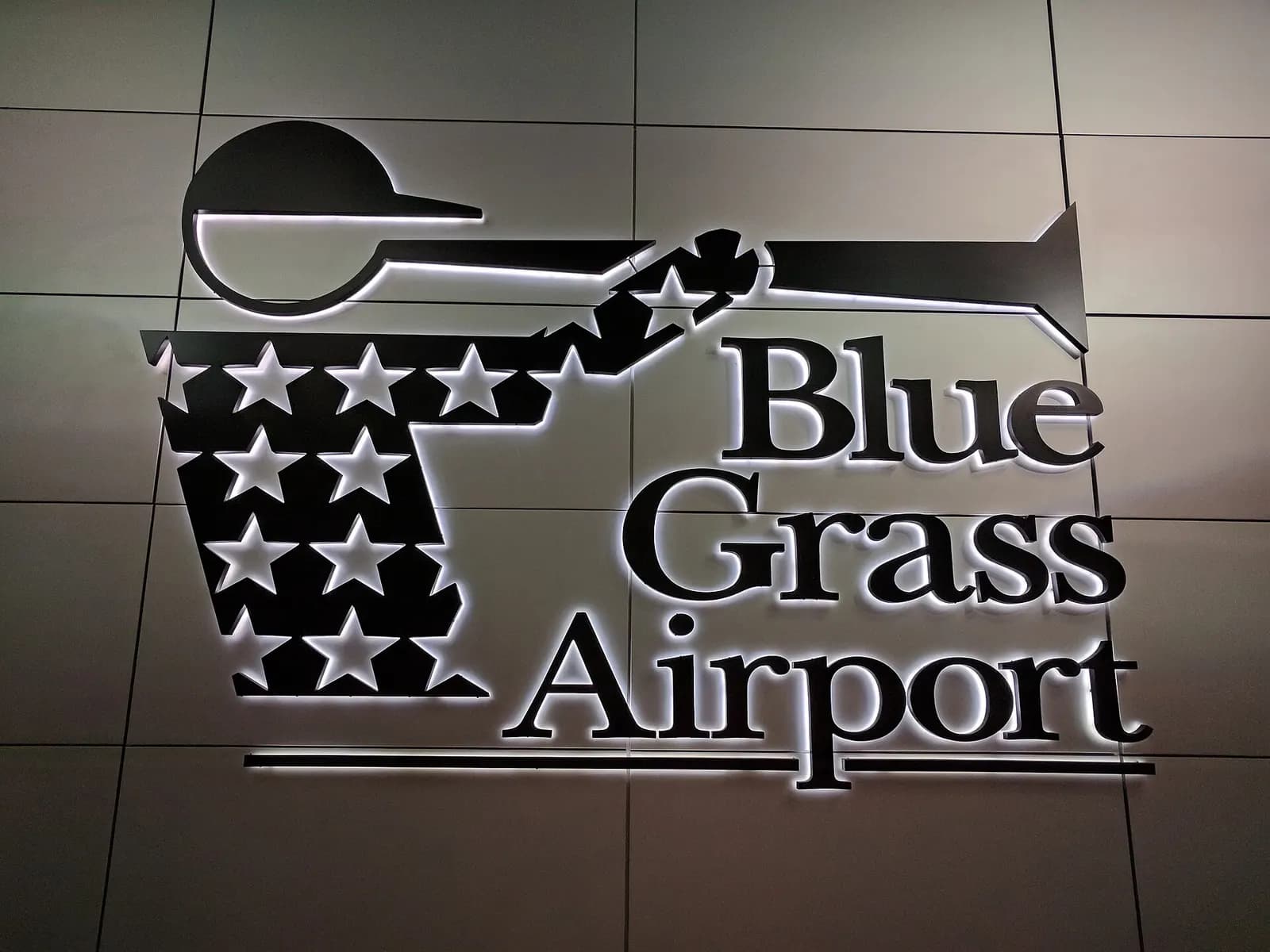 Illuminated bugler logo and Blue Grass Airport lettering next to a Terminal Lobby entrance, photographed in September 2017.