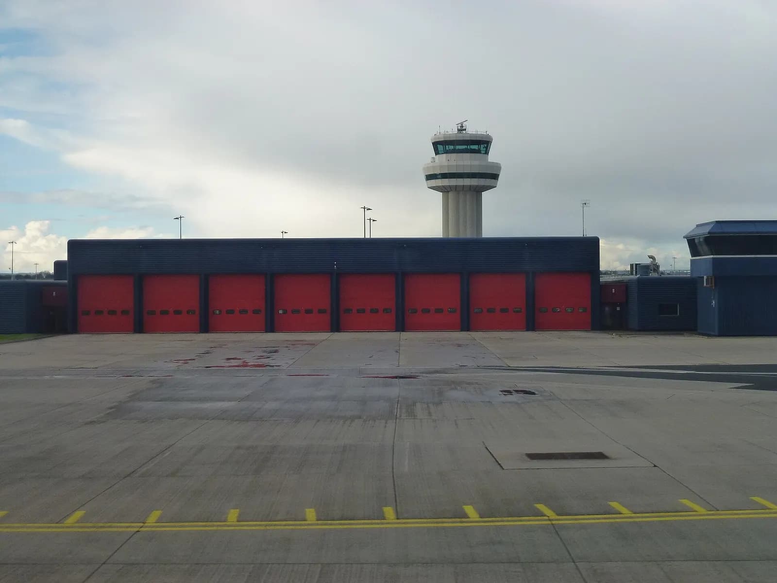 Gatwick Airport's air traffic control tower and fire station buildings against a cloudy sky.