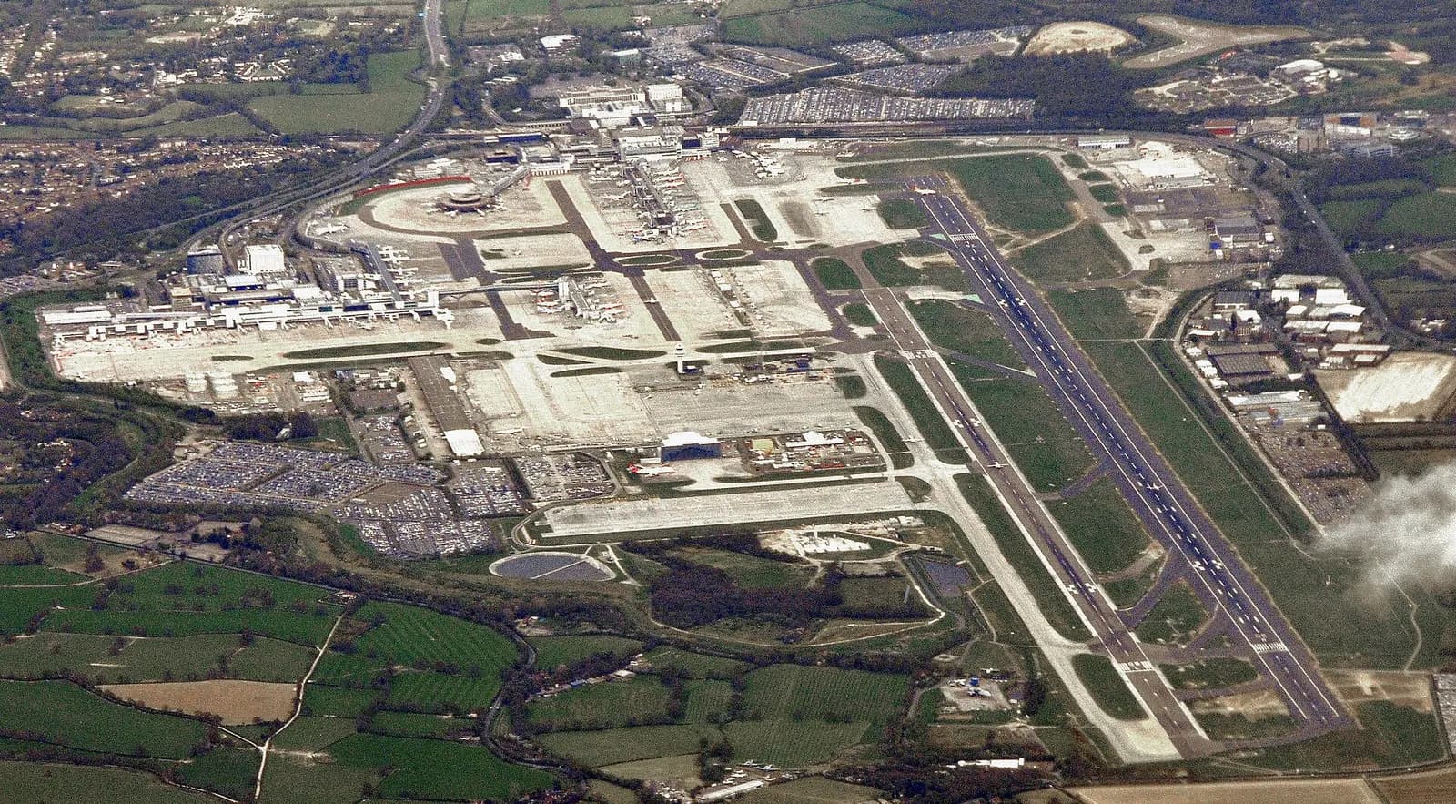 A wide view of London Gatwick Airport showing the main runway, taxiways, terminals, and surrounding landscape.