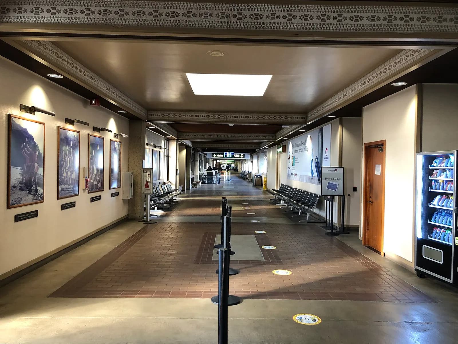 Interior corridor at Lihue Airport with framed photos, a vending machine, and holdroom seating