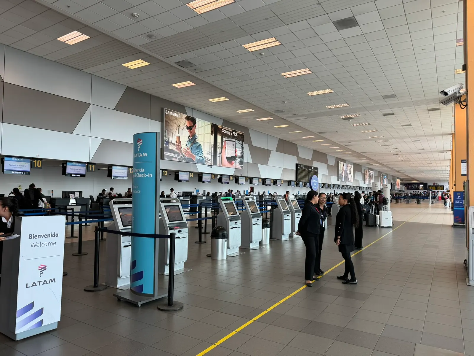 A row of LATAM airline check-in counters with digital displays and queuing lanes in the departures hall.