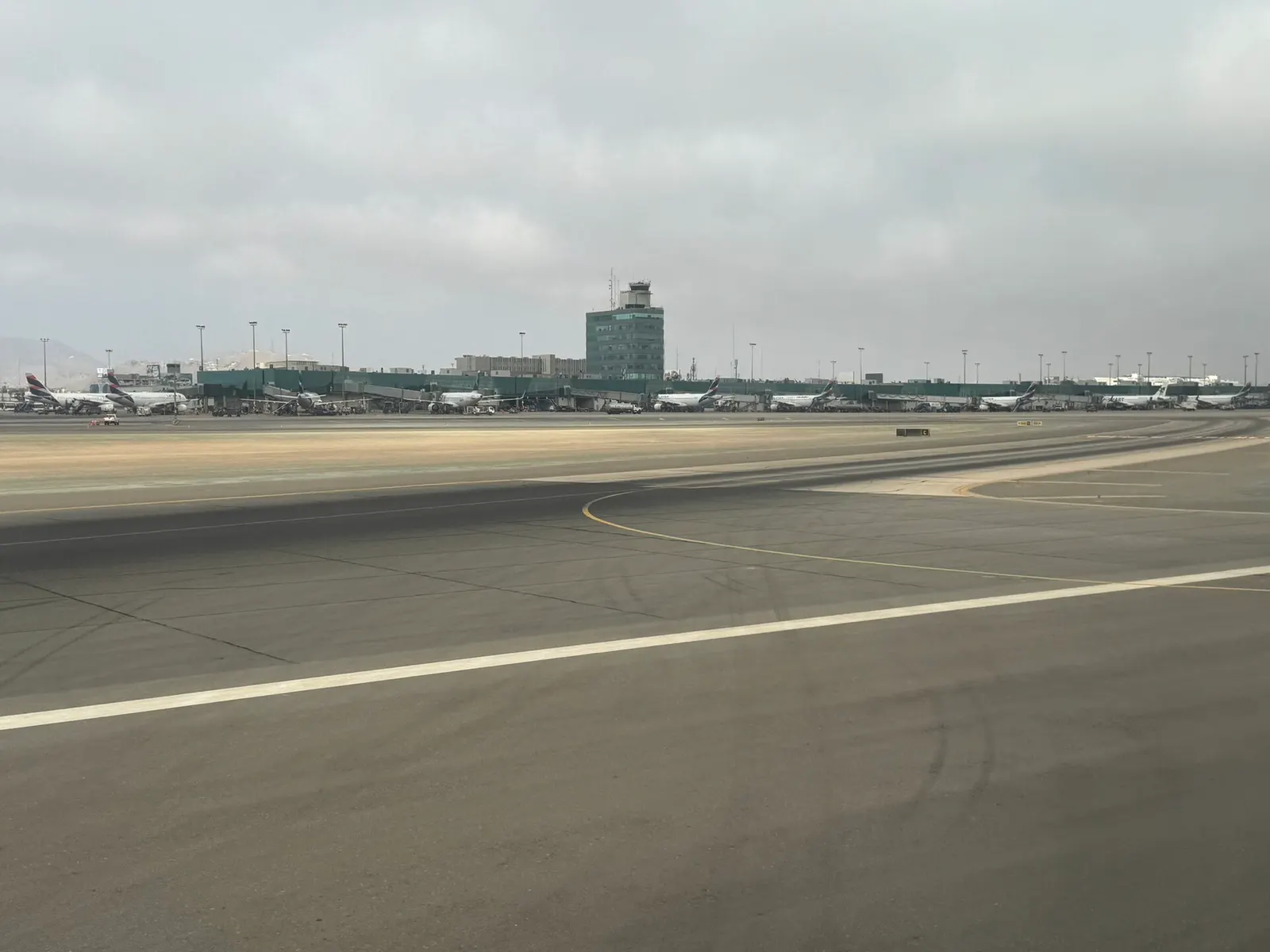 An airside view of the terminal ramps with parked commercial aircraft, jet bridges, and the main airport buildings.