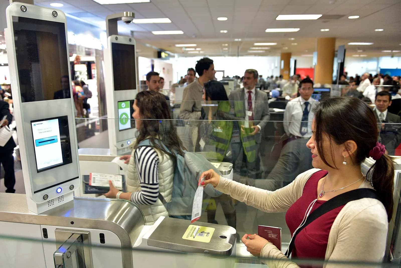 Travelers passing through automated biometric immigration gates with green indicator lights at Jorge Chávez International Airport.