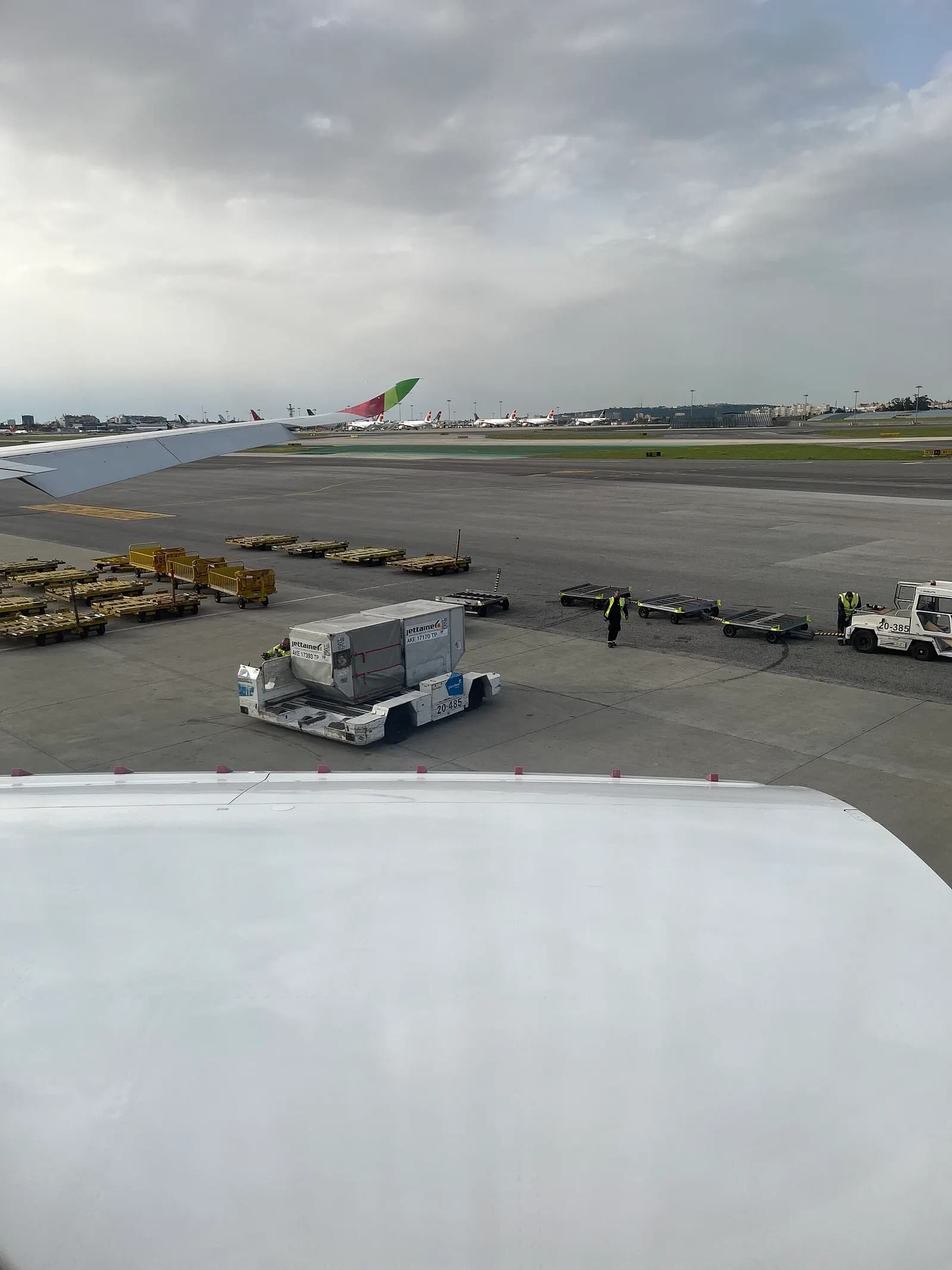 A view through terminal windows onto the airport apron with parked aircraft, jet bridges, and ground vehicles.