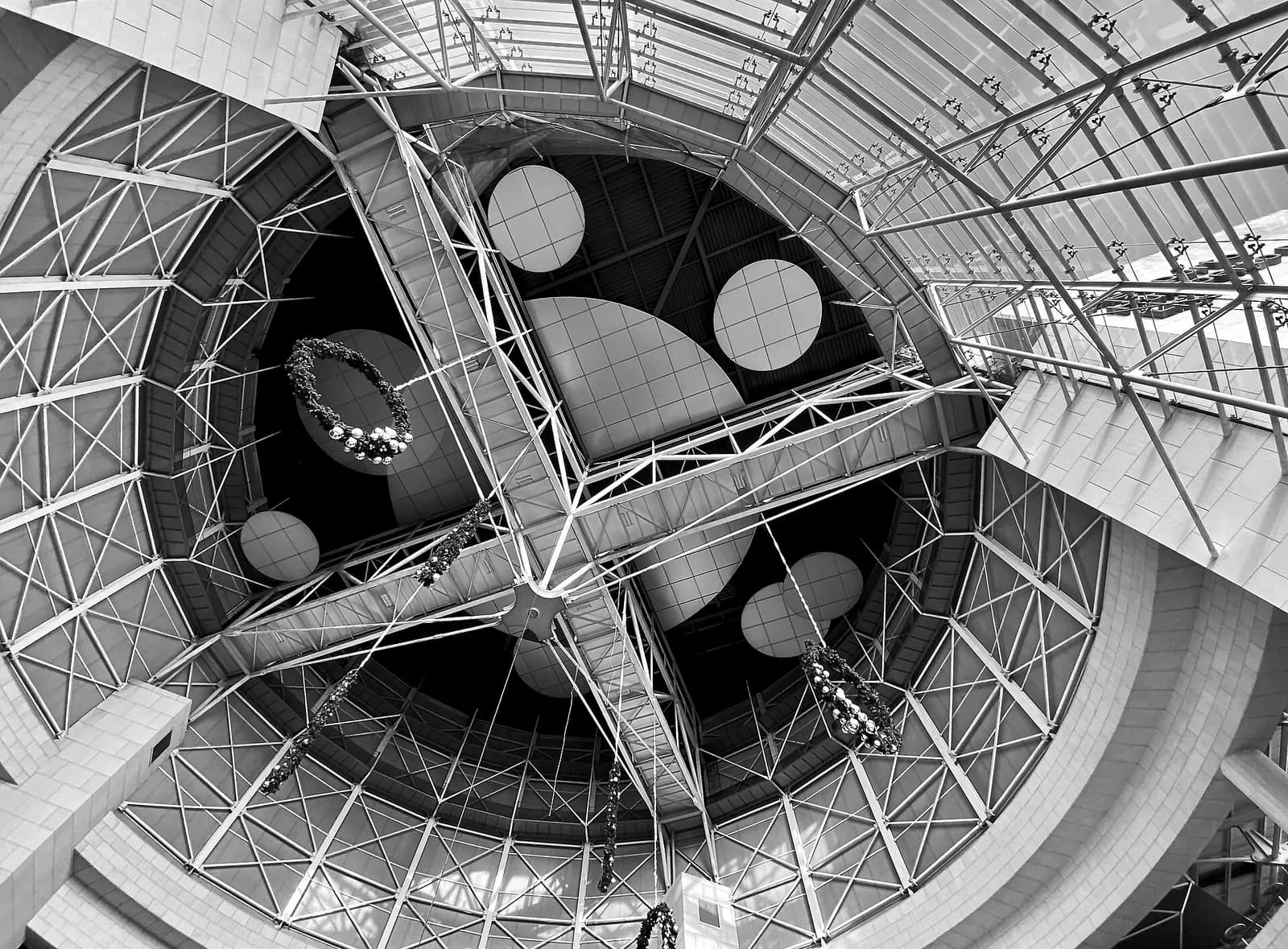 The patterned ceiling and upper level of a busy Terminal 1 departure lounge filled with seated travelers.