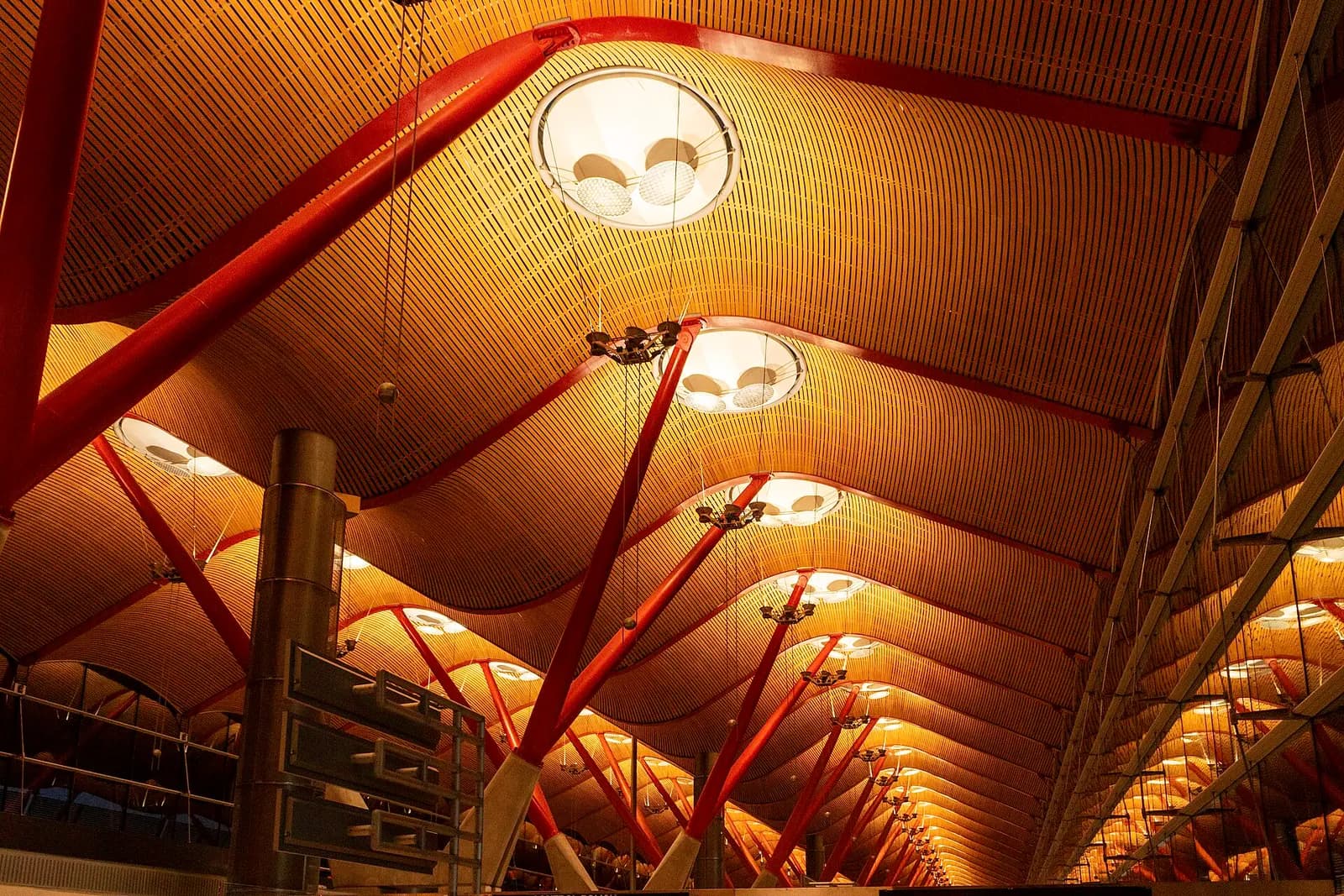 Inside Terminal 4, looking up at the high vaulted ceiling with exposed steel beams, wooden panels, and rows of skylights.