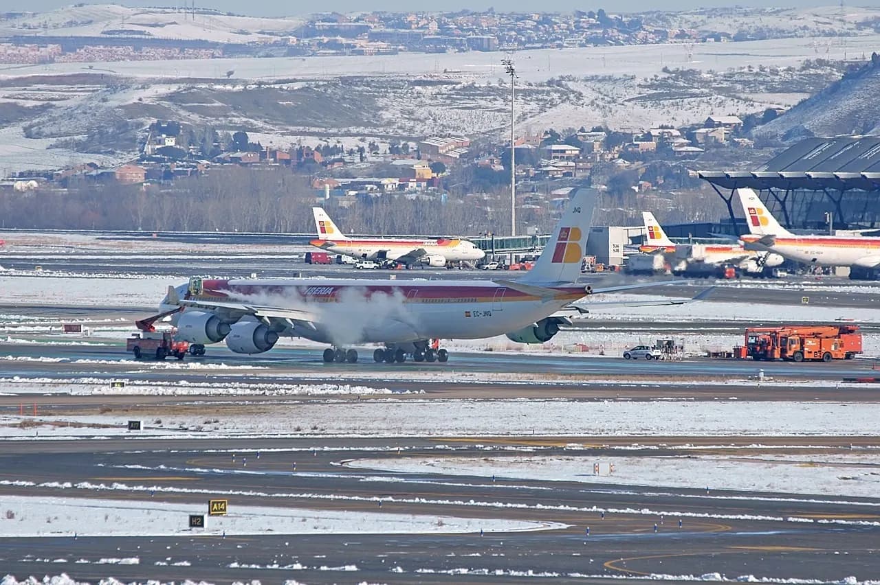 A winter view across snow-dusted fields toward runway 36L and the Terminal 4S satellite building in the distance.