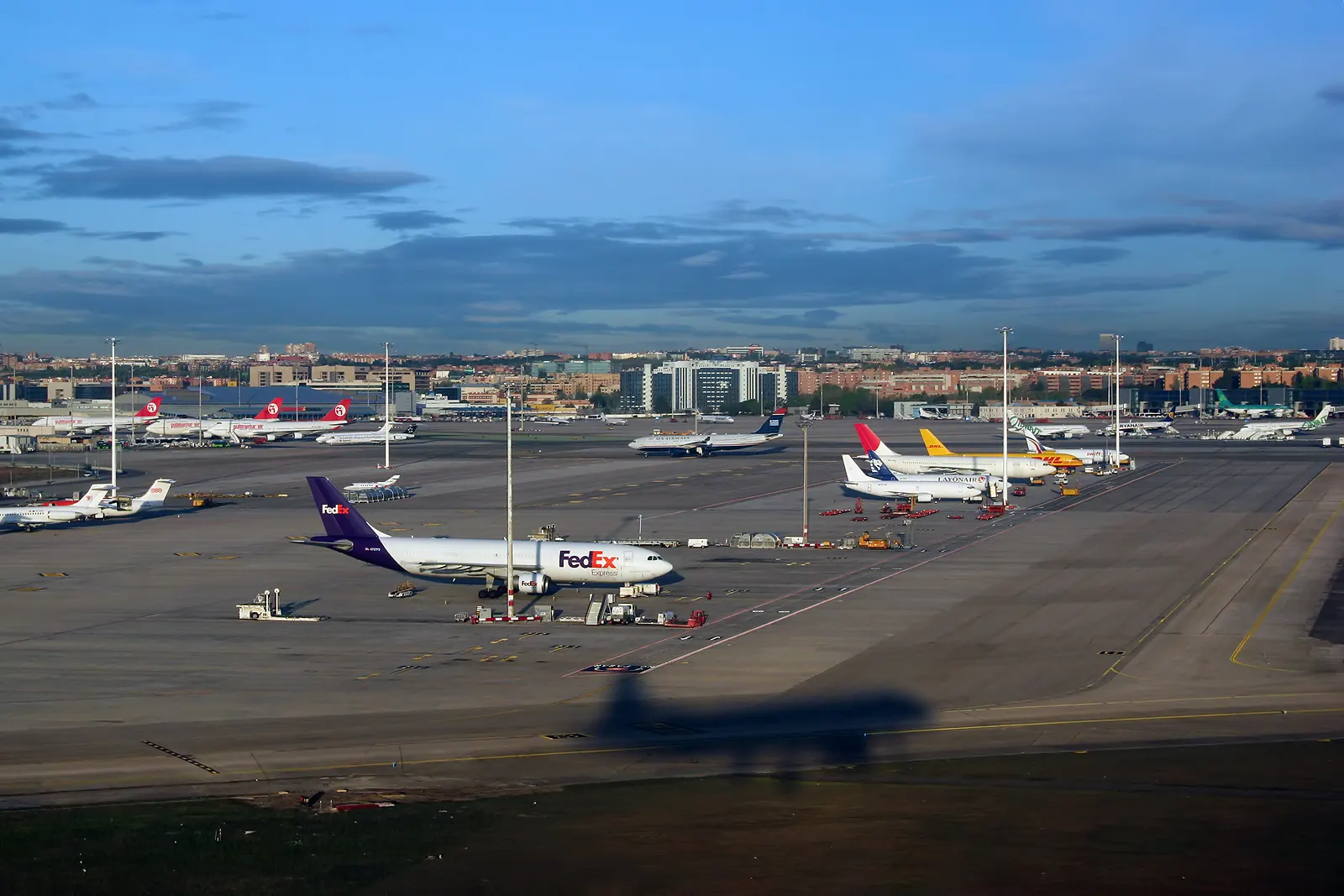 An aerial view on final approach showing Madrid–Barajas runways, taxiways, and terminal buildings spread across the plateau.