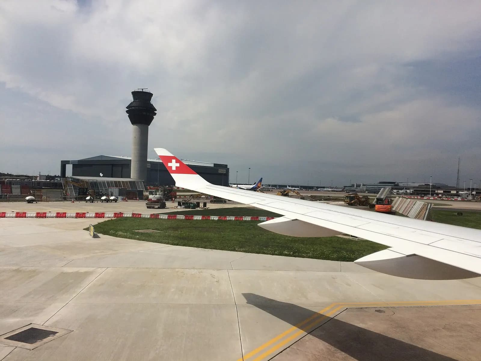 Tall modern air traffic control tower at Manchester Airport rising above the airfield under a cloudy sky.