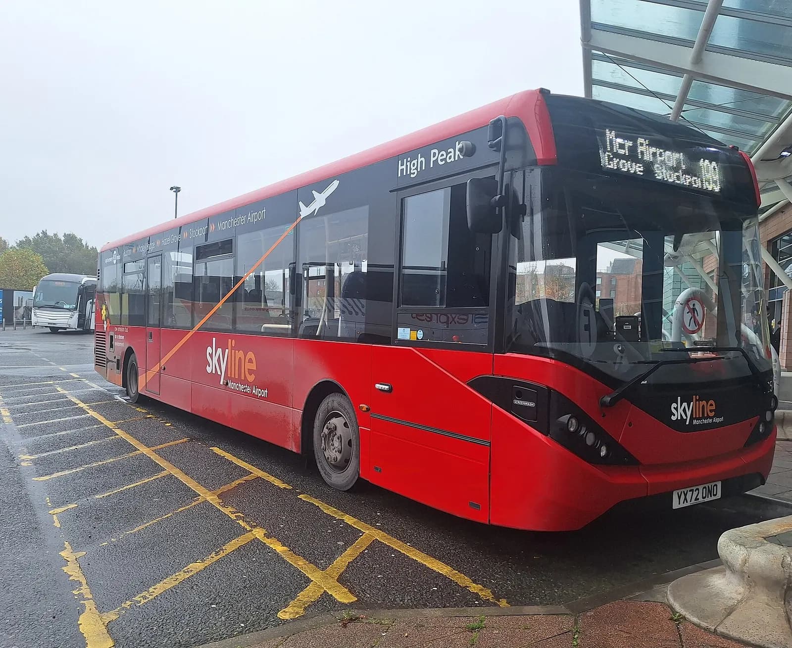High Peak route 199 bus at Manchester Airport with terminal buildings visible behind the stop.