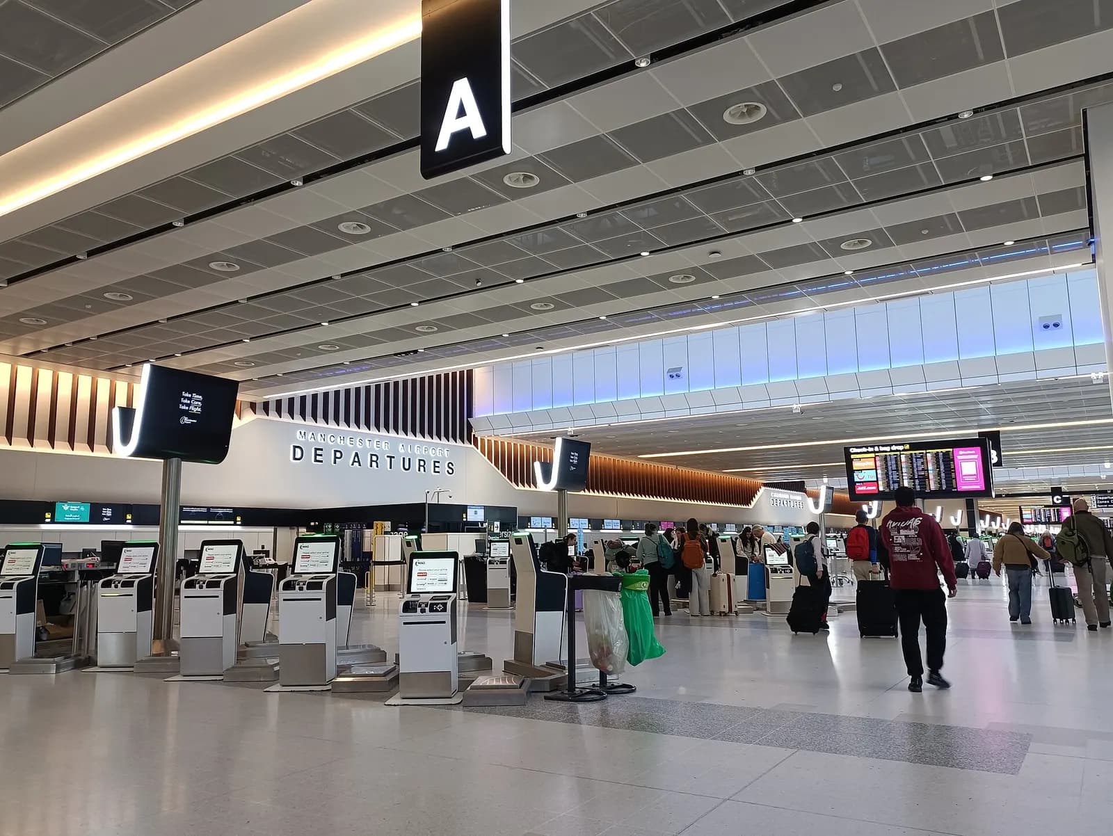 Bright, spacious refurbished departure hall in Manchester Airport Terminal 2 with check-in desks, seating areas, and floor-to-ceiling glass walls.