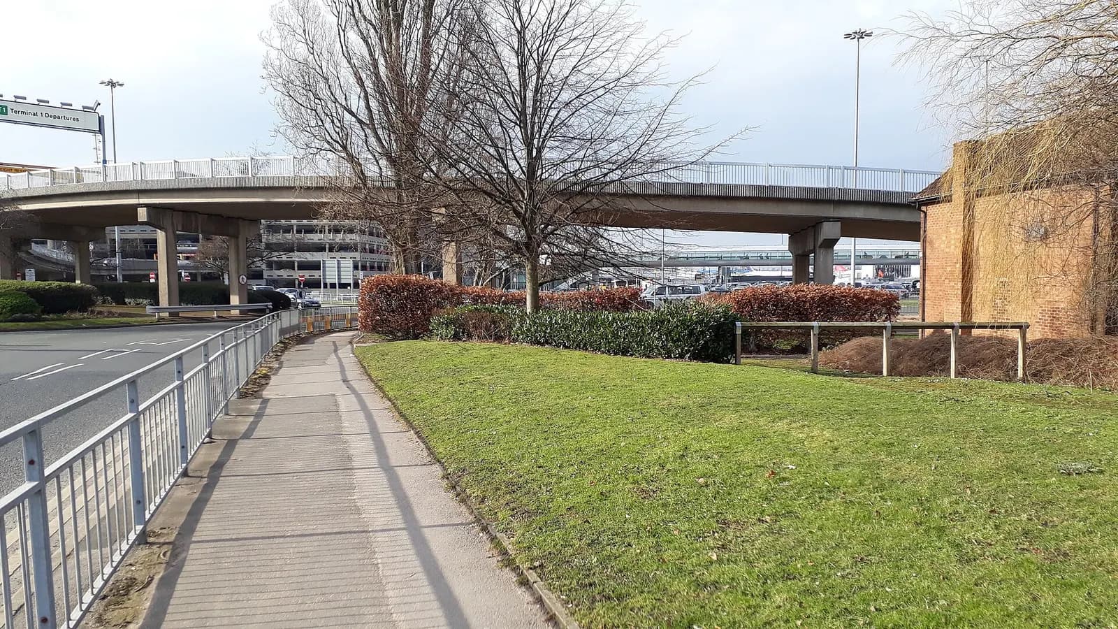 Airside departure concourse in Manchester Airport Terminal 1 with retail units, seating, and passengers walking toward the gates.