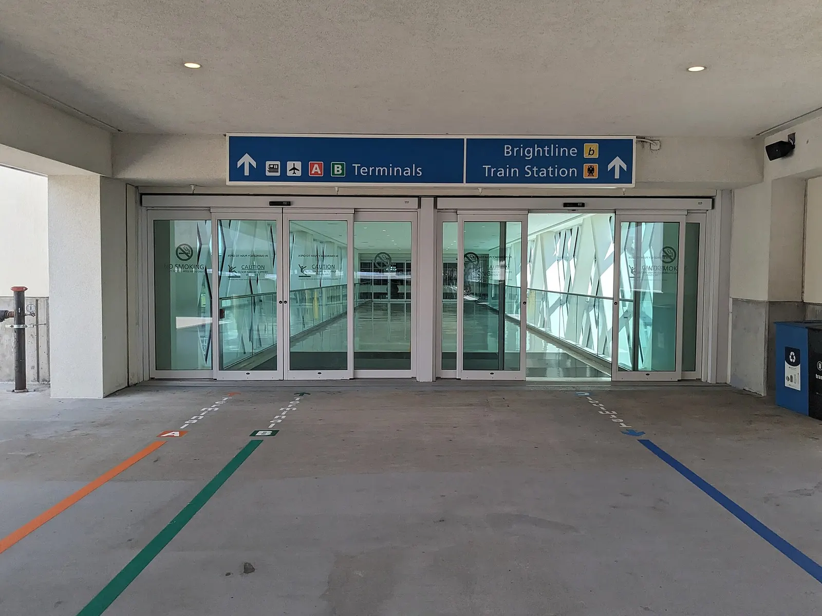 The walkway entrance from the parking garage into Orlando International Airport, with overhead signs pointing to Terminals A and B and to the Brightline train station.