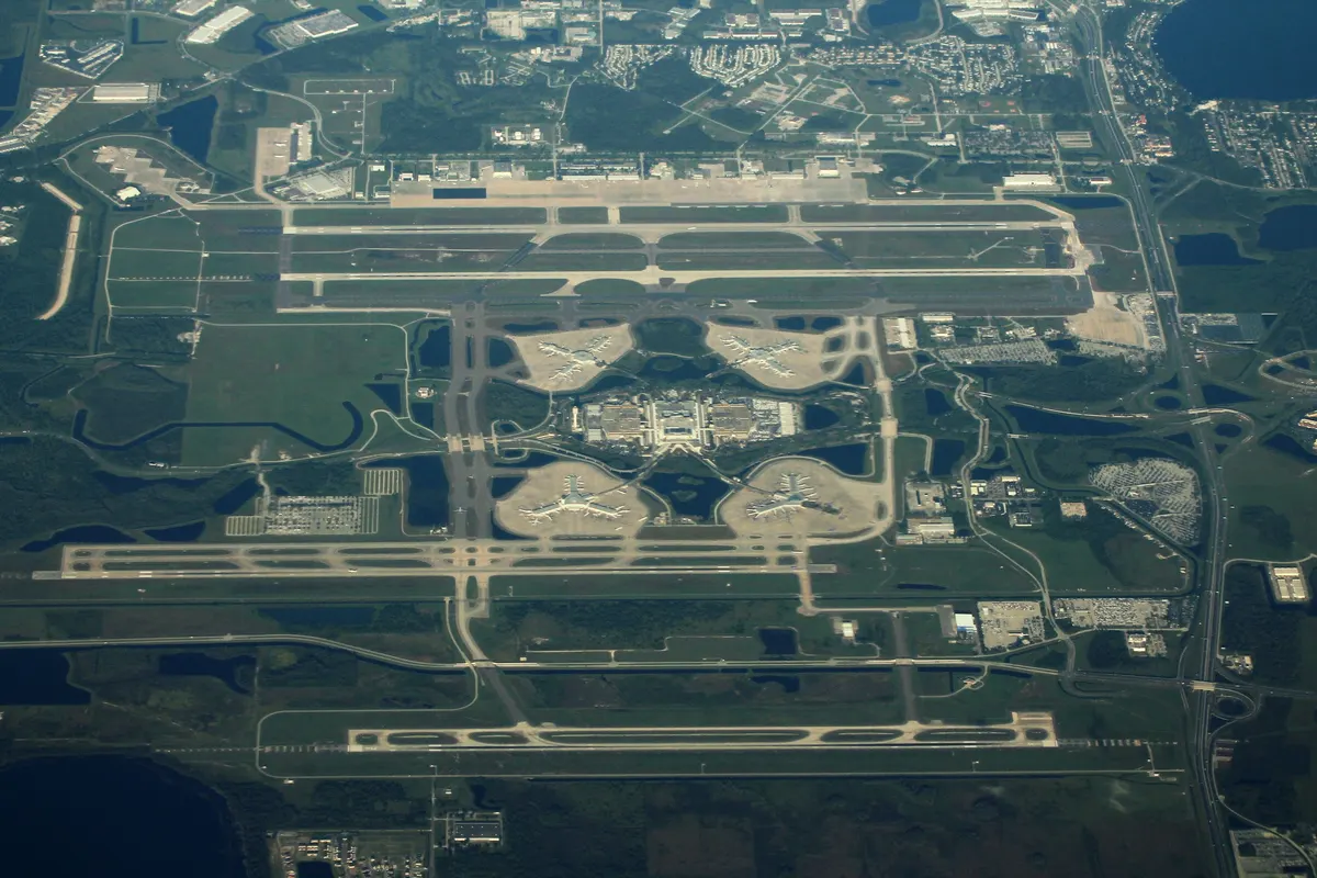An aerial view of Orlando International Airport showing parallel runways, terminal buildings, parking lots, and surrounding Central Florida landscape.