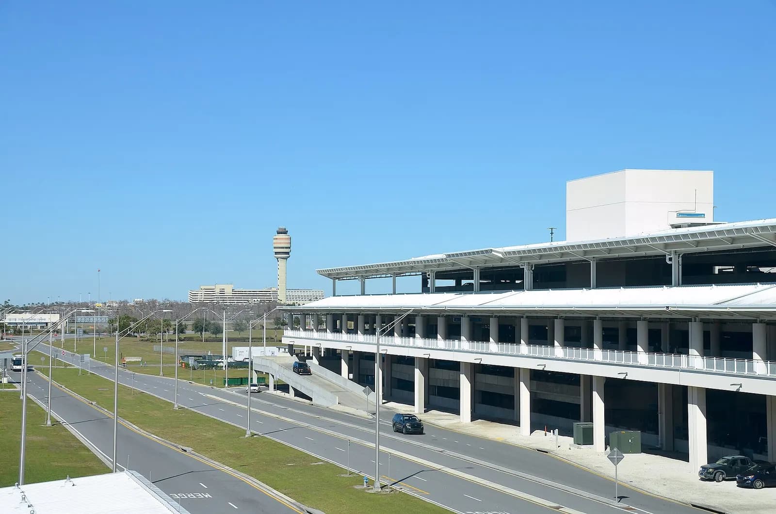 The Terminal C parking garage and air traffic control tower at Orlando International Airport seen from ground level against a blue sky.