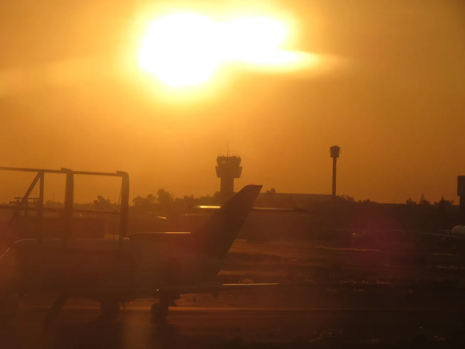 Air traffic control tower at Mexico City International Airport silhouetted against a pink and orange sunrise sky.