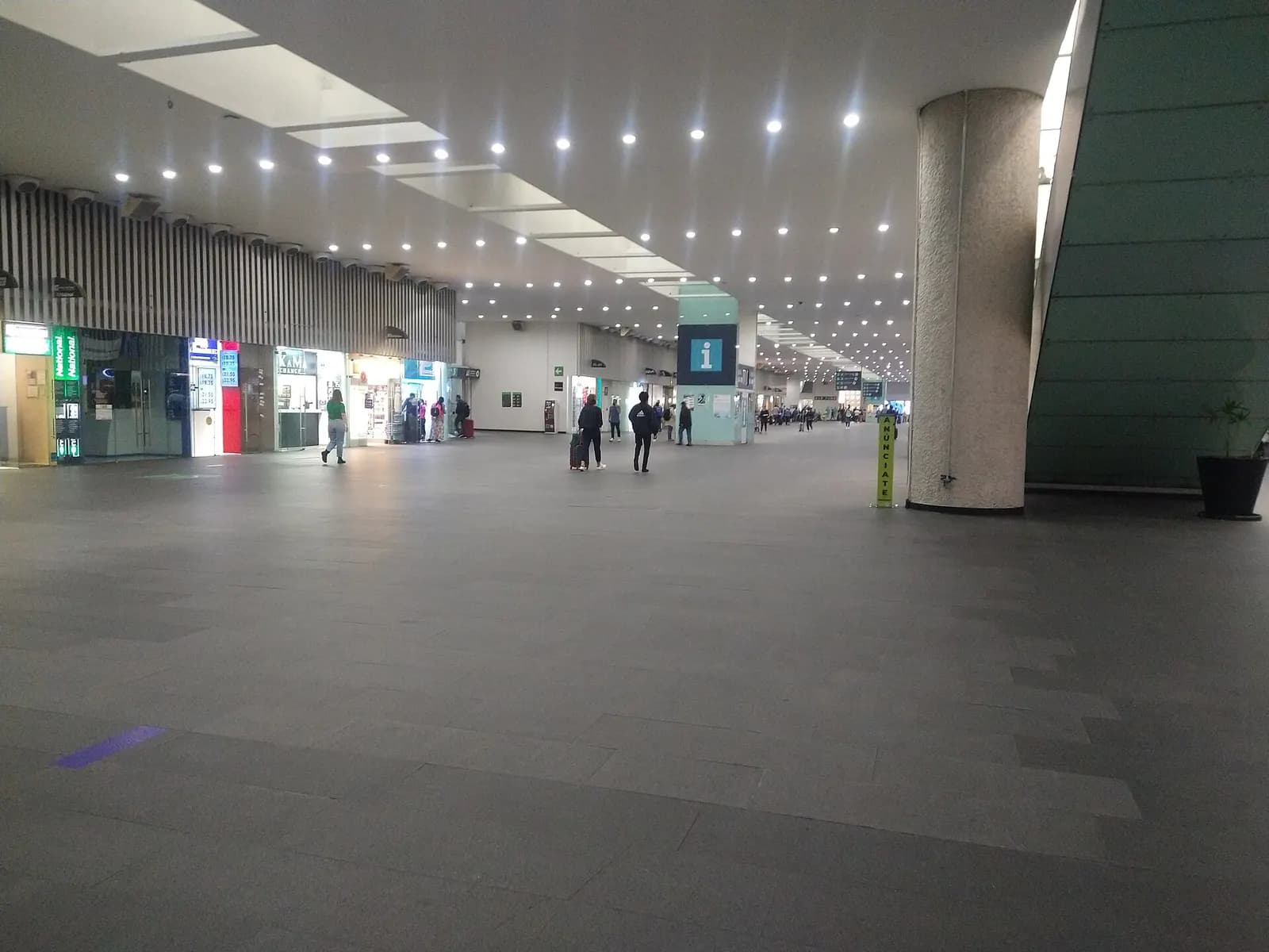 Spacious waiting hall in Terminal 2 with high ceilings, departure boards, passenger seating, and retail along the concourse.