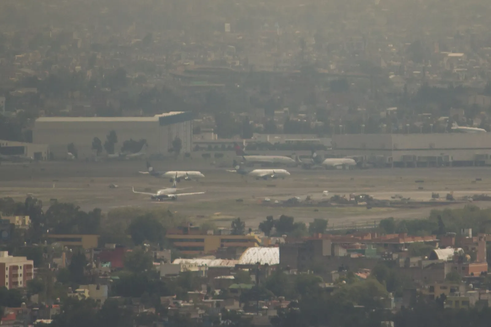 Wide view of Benito Juárez International Airport spread across the Mexico City basin, with runways, terminals, and the urban skyline in the background as seen from Torre Latinoamericana.