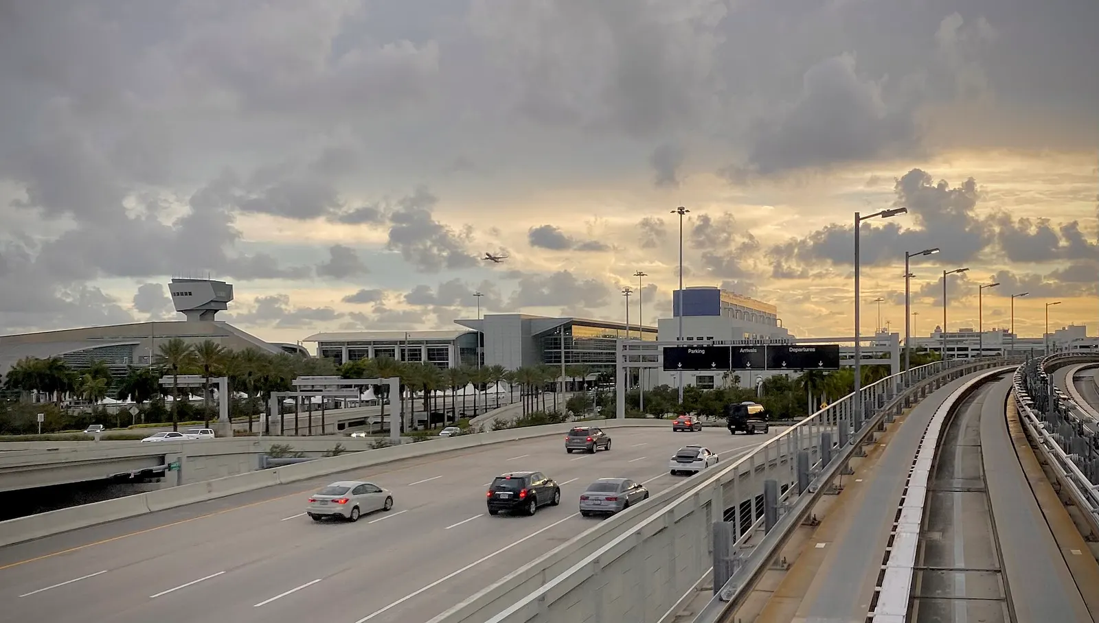 The main airport roadway at MIA with multiple vehicle lanes, terminal facades, and overhead directional signs.