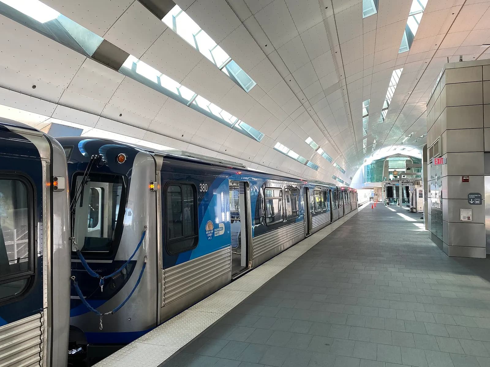 The Airport Metrorail station platform at MIA with Orange Line trains, railings, and transit signage.