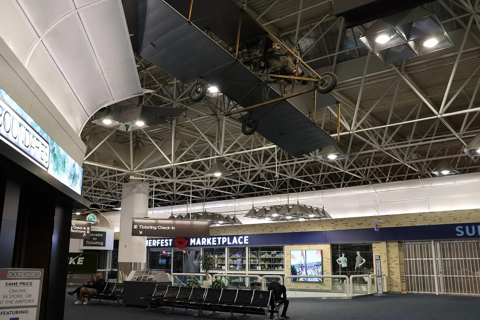 Main terminal hall with Summerfest Marketplace, a hanging Curtiss Pusher replica, and ticketing wayfinding.