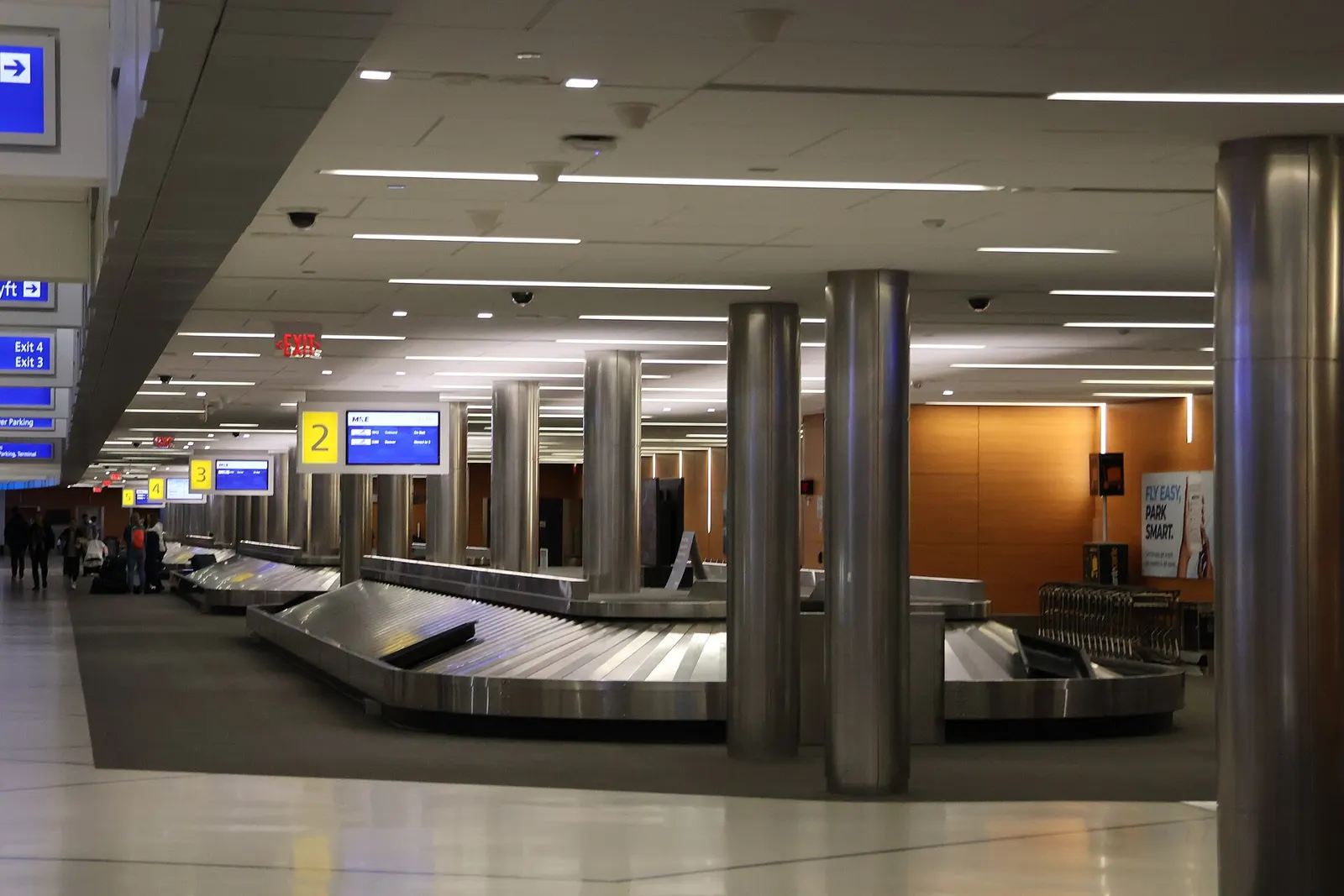 Baggage claim carousels 2–4 with an MKE arrivals board and Lyft / Exit 3–4 signs.