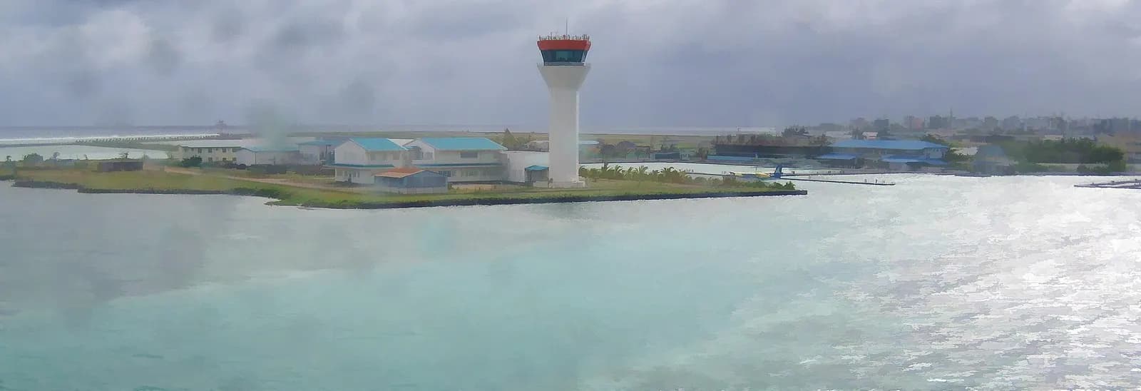 Waterfront panorama of Velana control tower and blue-roof airport buildings across turquoise water
