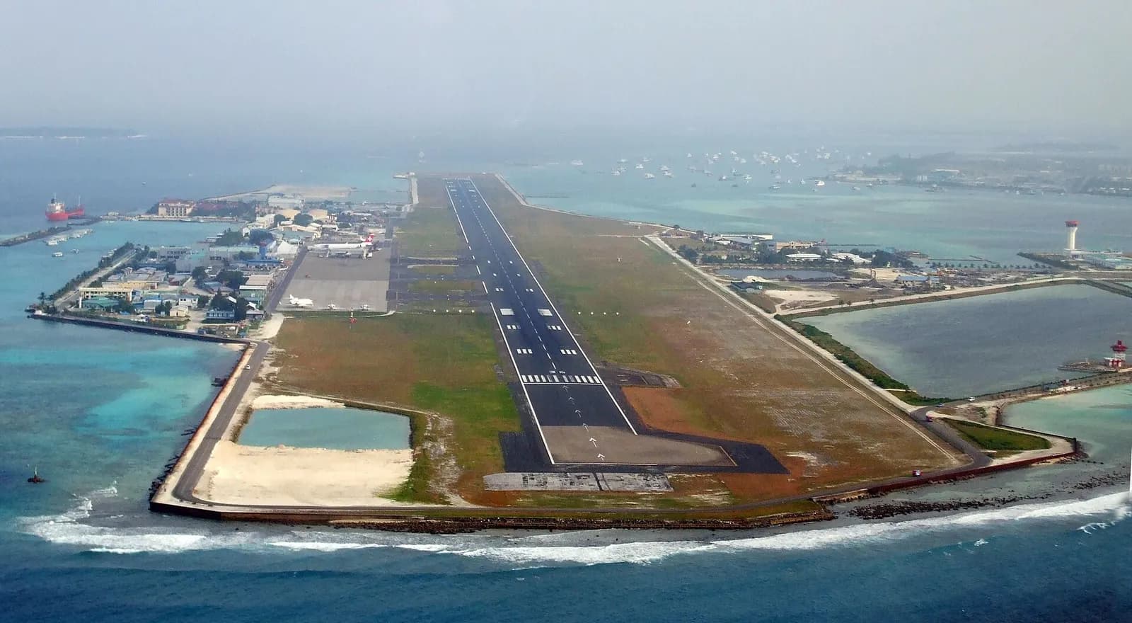Approach view over Velana International Airport runway, apron aircraft, and surrounding Maldivian islands