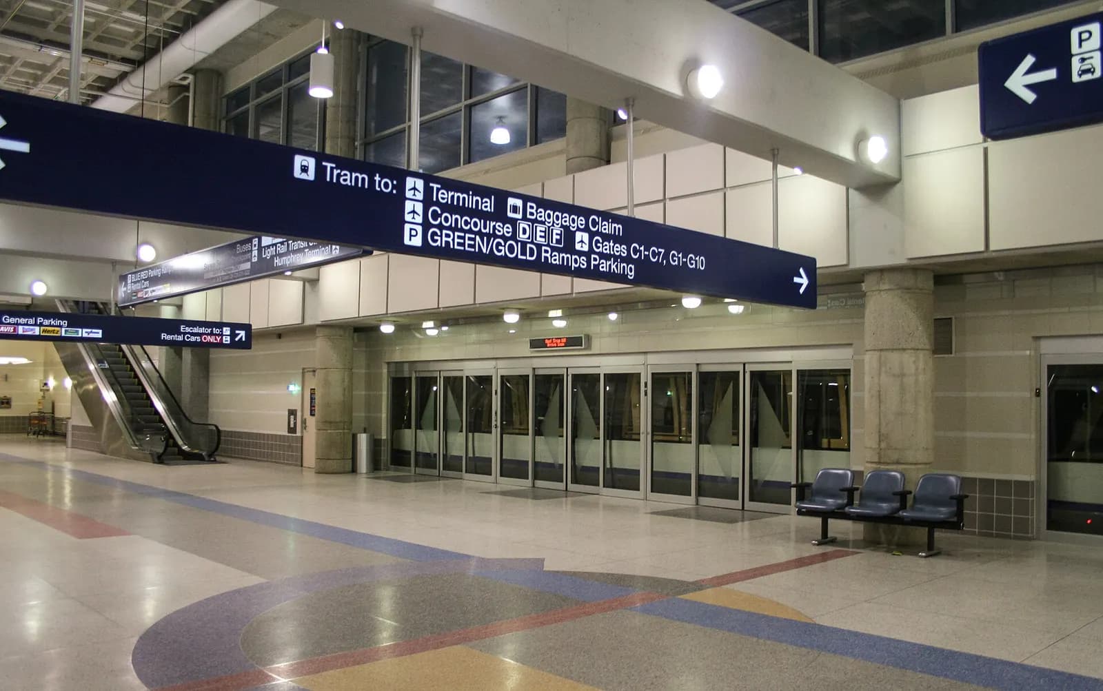The lower level of MSP's Terminal 1 showing the entrance to the inter-terminal tram with signage and a moving walkway.