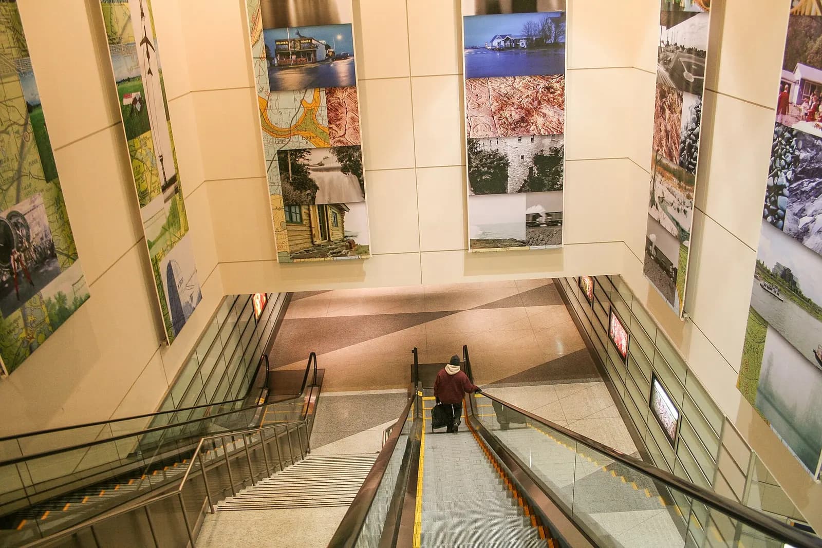 An escalator in the Minneapolis–Saint Paul airport terminal beside a colorful suspended art installation of geometric shapes and light.
