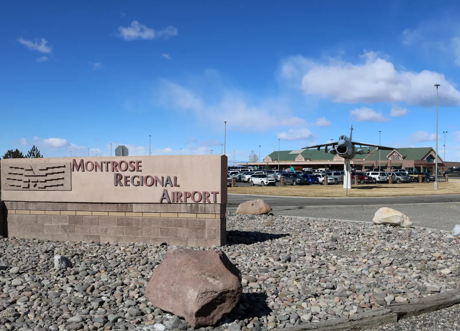 US-50 entrance sign at Montrose Regional Airport with the leftover A-7D static display and the passenger terminal behind it
