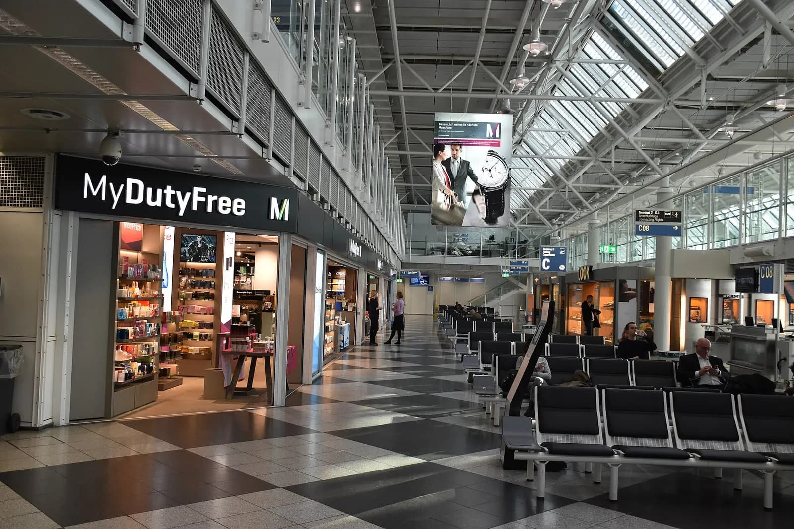 A wide, brightly lit concourse in Terminal 1 Module C with seating areas, shops, and gate corridors stretching into the distance.