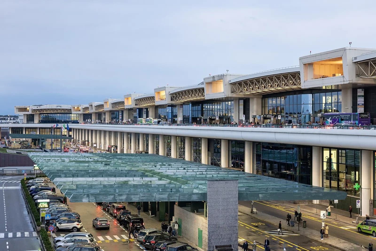 Terminal 1 at Milan Malpensa Airport with its tall control tower and curved glass facade under a clear sky.