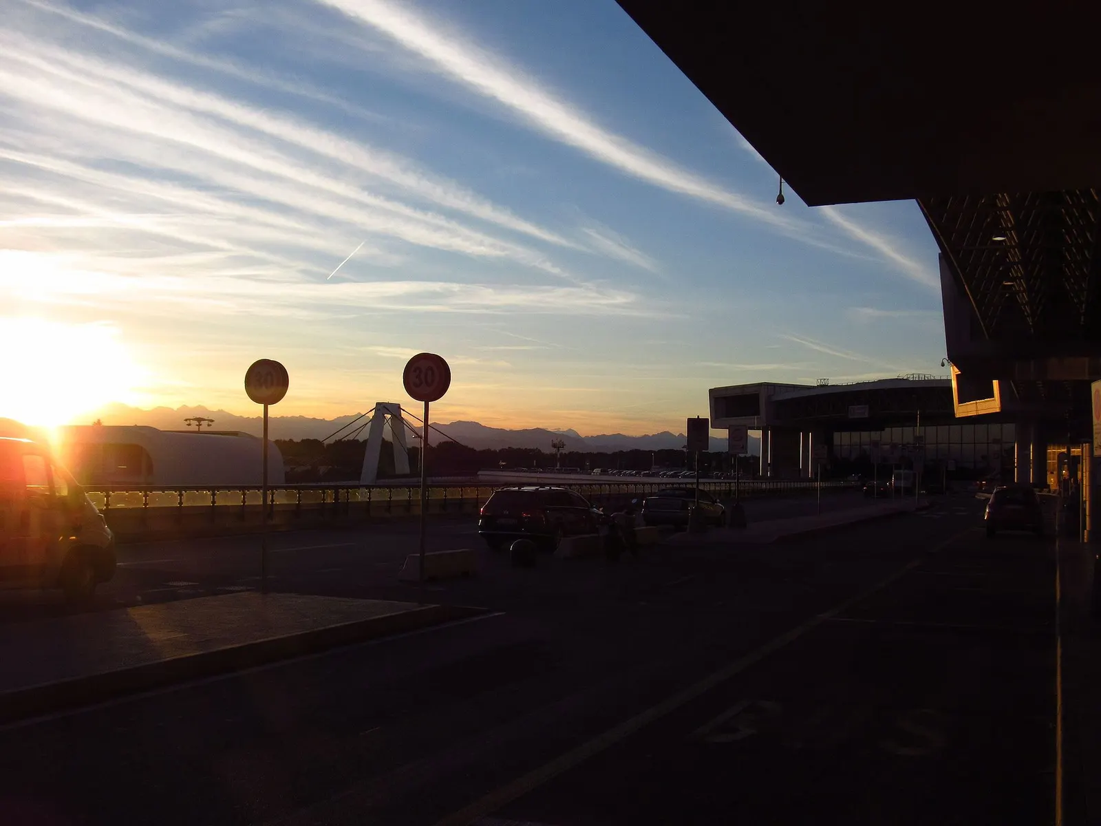Sunset light over Milan Malpensa Airport with warm colors above the terminal and surrounding airfield.