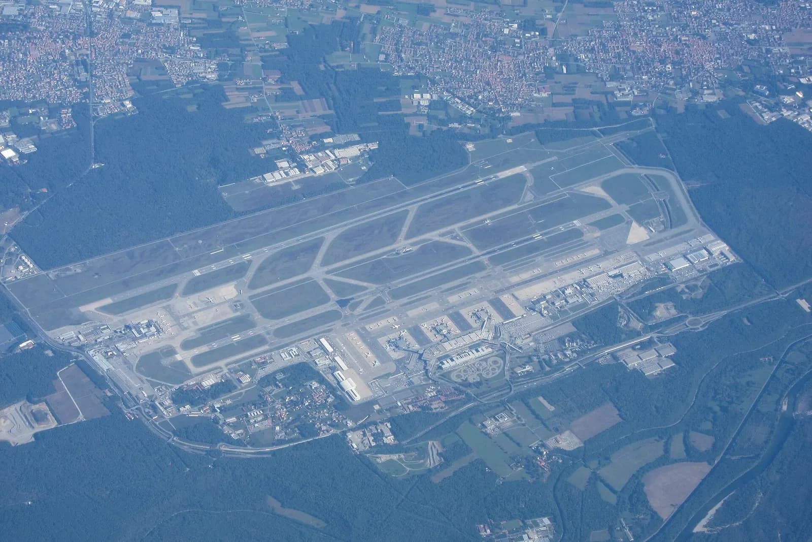 Aerial view of Milan Malpensa showing parallel runways, terminal buildings, and open countryside around the airfield.